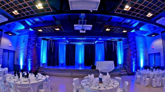 Salle de réception éclairée en bleu avec tables rondes dressées