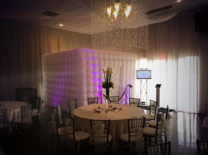 Cabine photobooth gonflable éclairée en violet dans une salle de réception aux tables dressées